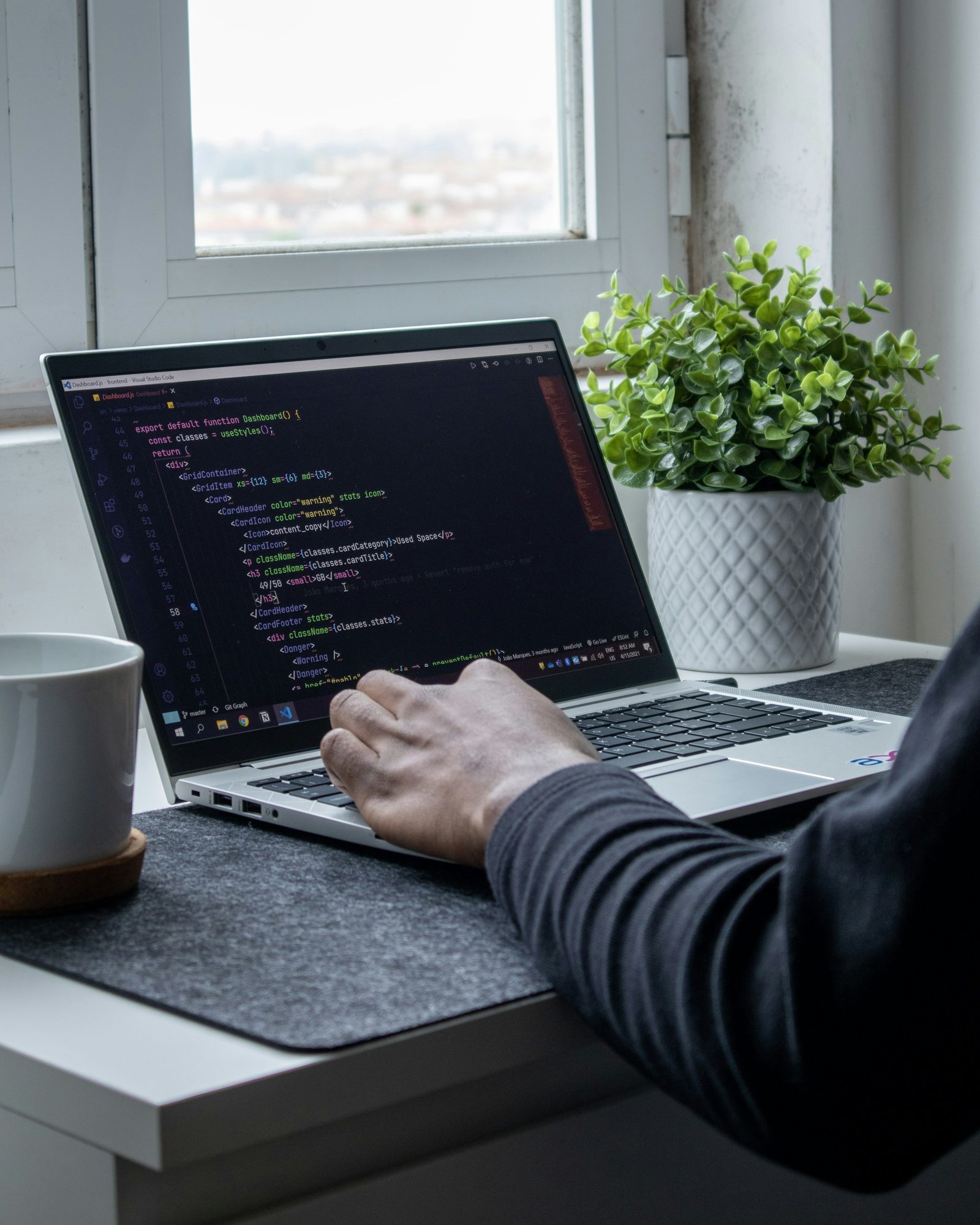 Hands at a laptop with code on the screen, beside a window