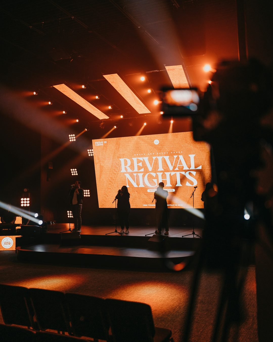 Church stage lit in orange with a wide screen showing event graphics behind a worship team